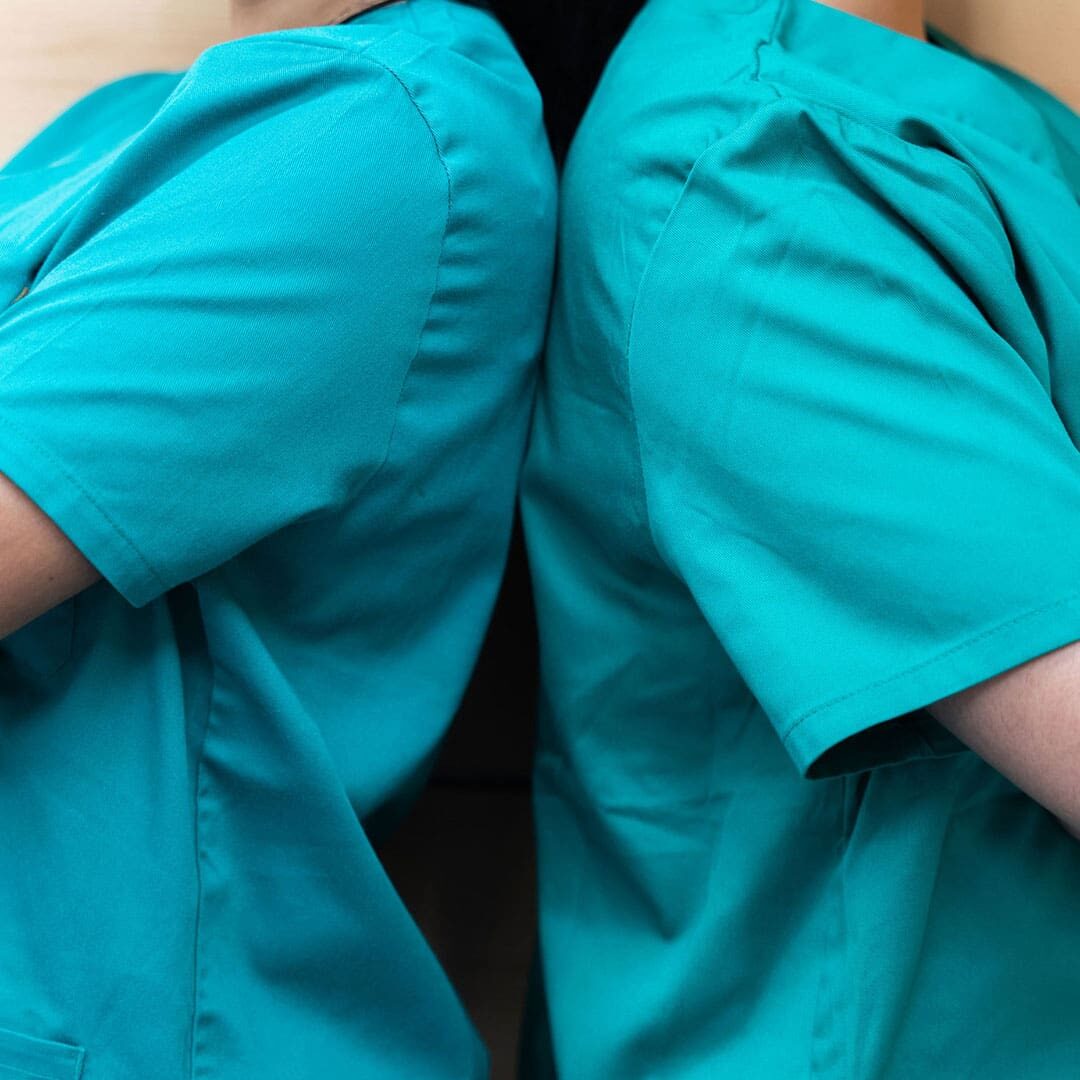 two veterinarians wearing blue scrub tops standing back to back